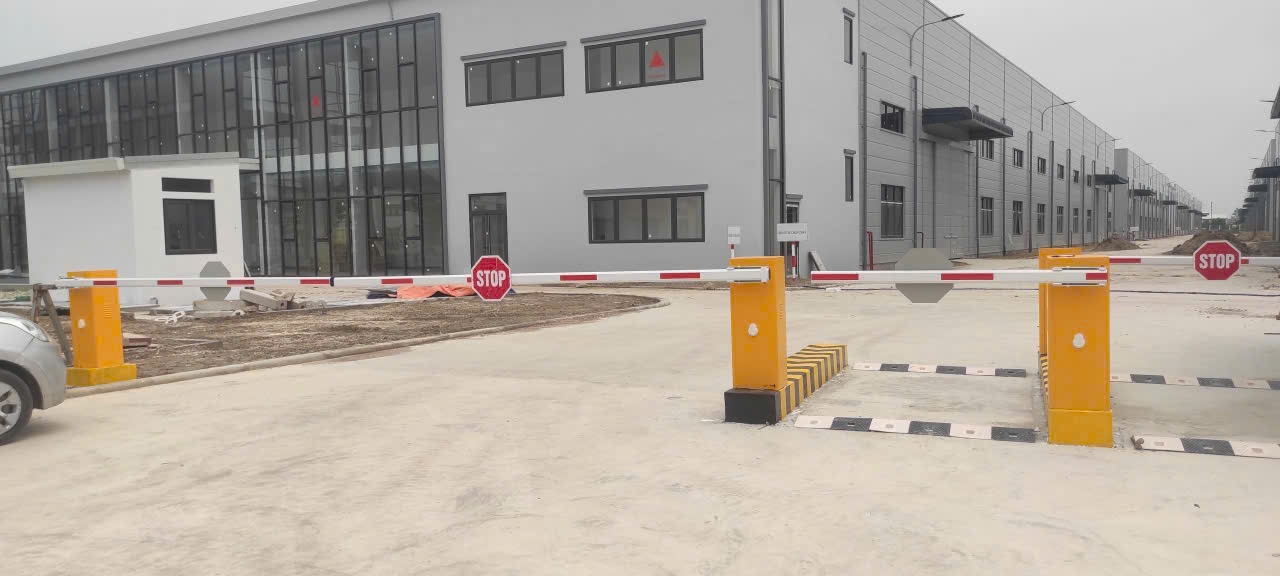 Thanh chắn barie tự động màu vàng tại cổng khu công nghiệp với biển báo dừng STOP